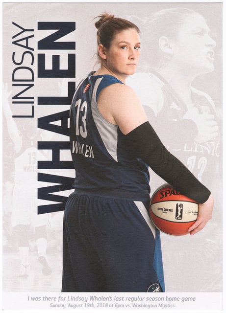 Basketball player in a gray-and-blue jersey and shorts holding a basketball with her back to the viewer, holding a basketball in her right hand.